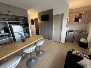 A compact kitchen with a wooden countertop, bar stools, a dishwasher, and a TV mounted on the wall.