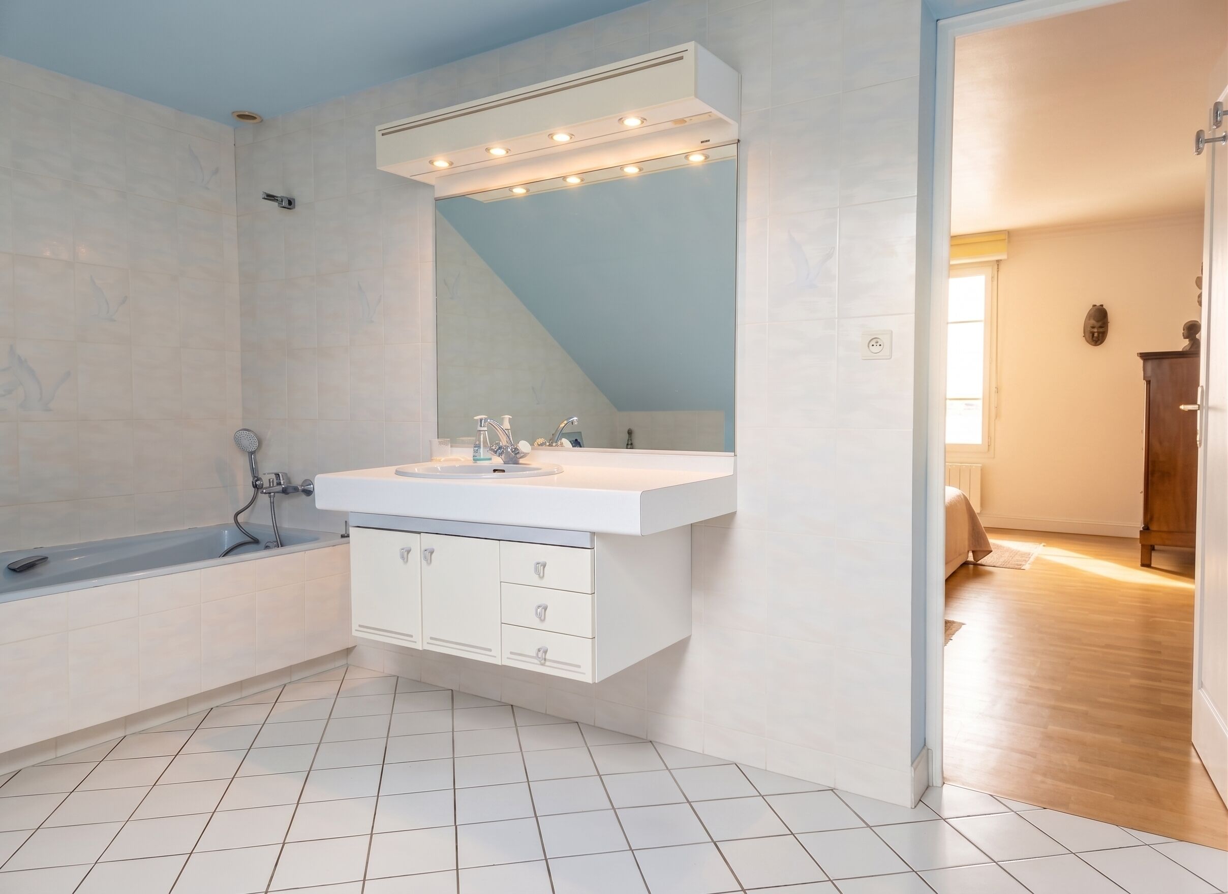 A modern bathroom with a white vanity, a large mirror, and a bathtub.