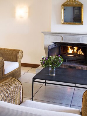 A room with a fireplace, wicker furniture, and a vase with flowers.
