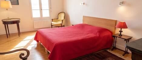 A bedroom with a bed, a chair, a lamp, a radiator, and a window.