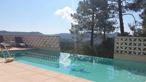 Ein Schwimmbecken mit Bergblick, umgeben von einem weißen Gitterzaun und Liegestühlen.