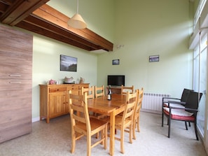 A dining area with a wooden table and chairs, a television, and a window with blinds.