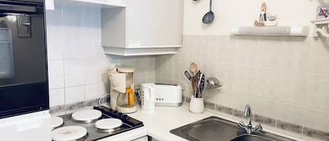 Una cocina con estufa, cafetera, tostadora, lavabo y un reloj de pared.