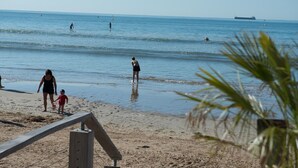 Een strand met mensen die wandelen en zwemmen, een houten omheining en een schip in de verte.