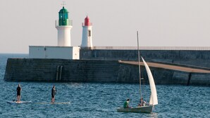Een kustlandschap met een vuurtoren, een pier en mensen die watersporten beoefenen.