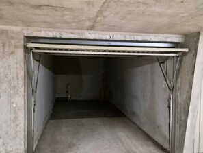 A concrete interior space with a metal door, a metal beam overhead, and a concrete floor.