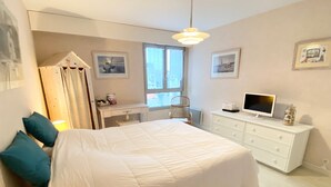 Een slaapkamer met een groot bed, een bureau, een stoel, een televisie en een raam.