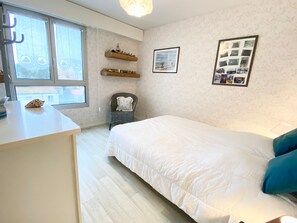 A bedroom with a bed, a chair, a small table, and a window.