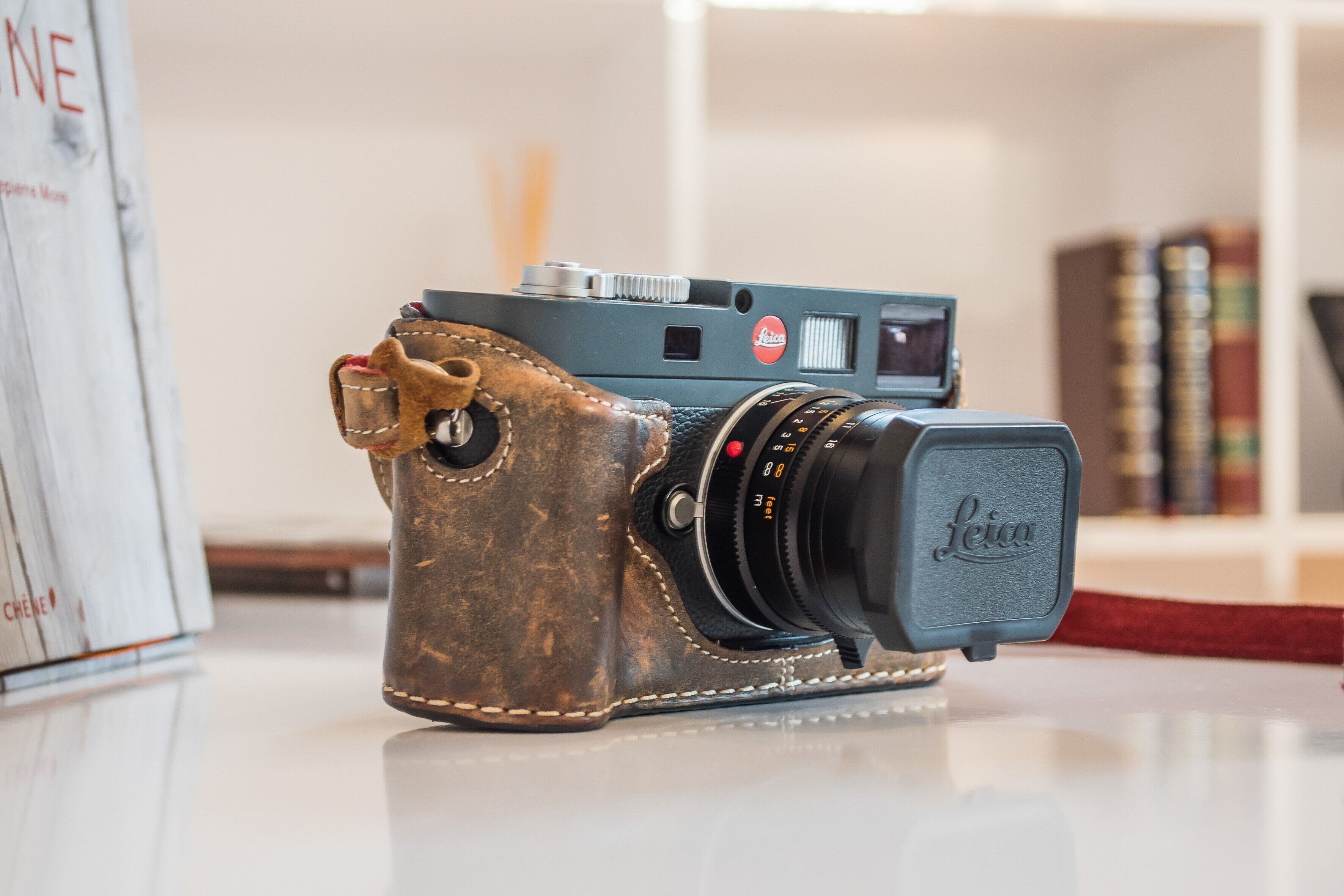 Een oude Leica camera met leren bandjes, geplaatst op een reflecterend oppervlak met boeken op de achtergrond.
