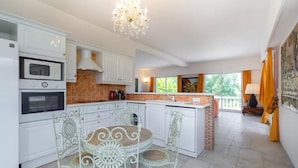 A modern kitchen with white cabinetry, a dining area with a white table and chairs, and a large window providing a view of the outdoors.