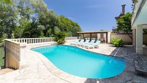 A swimming pool with lounge chairs, surrounded by a stone patio and trees.