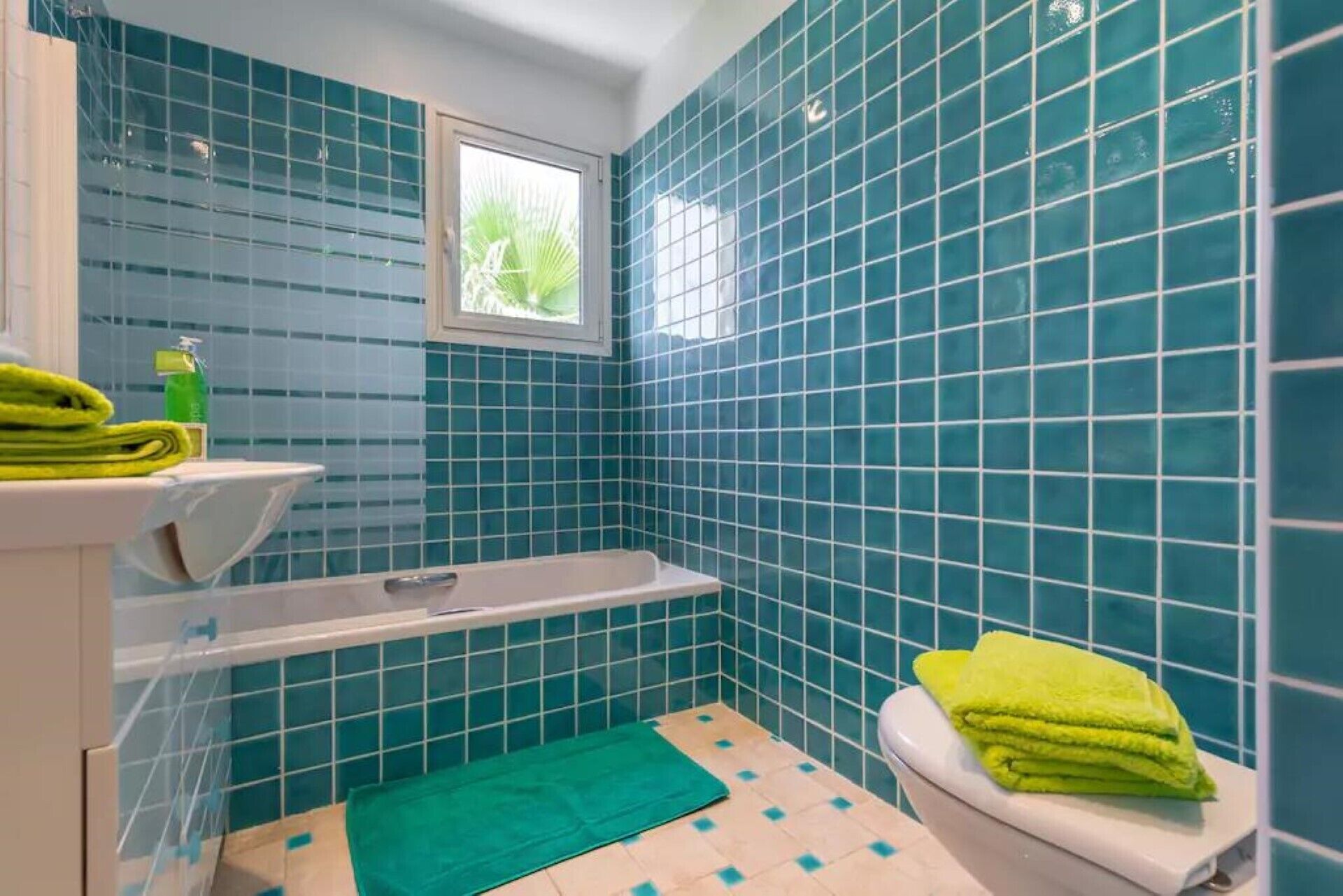Un baño con azulejos azules, una ventana, un inodoro y una bañera.