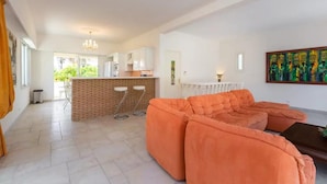 A spacious living area with a large orange sofa, a kitchen with white cabinets, and a dining area with a brick accent wall.