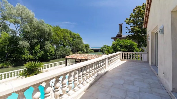 A balcony with a tiled floor, a white balustrade, and a view of a river and trees.