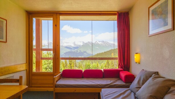 A room with a bed, a wooden bench, a table, and a window with a mountain view. - Ski-in studio, 5 pax, pets allowed, Arc 1800 (Les Arcs 1800)