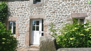 Un edificio de piedra con una puerta blanca, dos ventanas y un pequeño balcón.