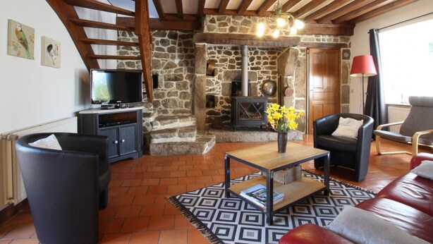 Una sala de estar acogedora con chimenea de piedra, vigas de madera, televisor y asientos cómodos.
