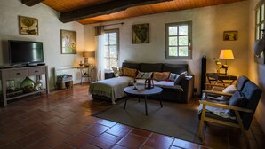 A cozy living room with a sofa, armchairs, a coffee table, and a television. There are windows, a fireplace, and artwork on the walls. - L' OUSTAOU LES FORTUNES 3-star Provence farmhouse (Ansouis)