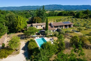 A villa with a swimming pool, surrounded by lush greenery and vineyards, with a view of distant mountains. - L' OUSTAOU LES FORTUNES 3-star Provence farmhouse (Ansouis)