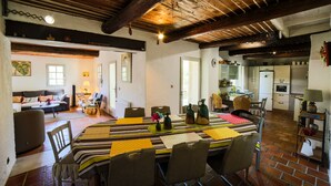 A spacious living area with a dining table, chairs, and a kitchen in the background. - L' OUSTAOU LES FORTUNES 3-star Provence farmhouse (Ansouis)