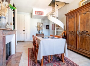A dining area with a white table, chairs, and a patterned rug. There is a wooden cabinet and a spiral staircase in the background. - Homerez - Apt. central Saumur, city view (Saumur)