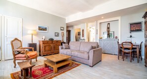A living room with a sofa, a wooden coffee table, a patterned rug, a wooden cabinet, and a chair. - Homerez - Apt. central Saumur, city view (Saumur)