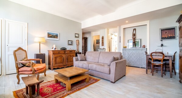 A living room with a sofa, a wooden coffee table, a patterned rug, a wooden cabinet, and a chair. - Homerez - Apt. central Saumur, city view (Saumur)