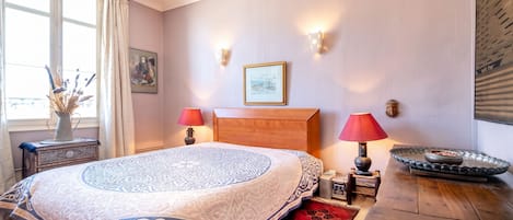 Un dormitorio con una cama grande, dos lámparas de noche, un cabecero de madera, un cuadro en la pared y una mesita con un cuenco.