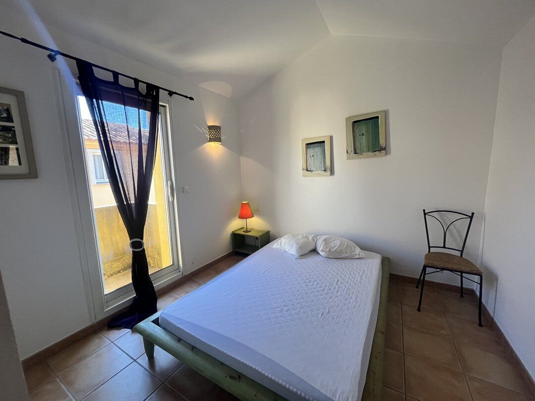Un dormitorio con una cama, una silla, una mesita de noche con lámpara y dos cuadros en la pared.