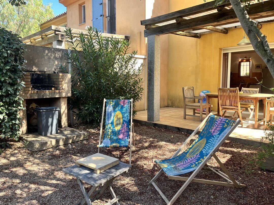 Une terrasse extérieure équipée d’un barbecue, de deux chaises longues et d’un coin repas avec des meubles en bois.