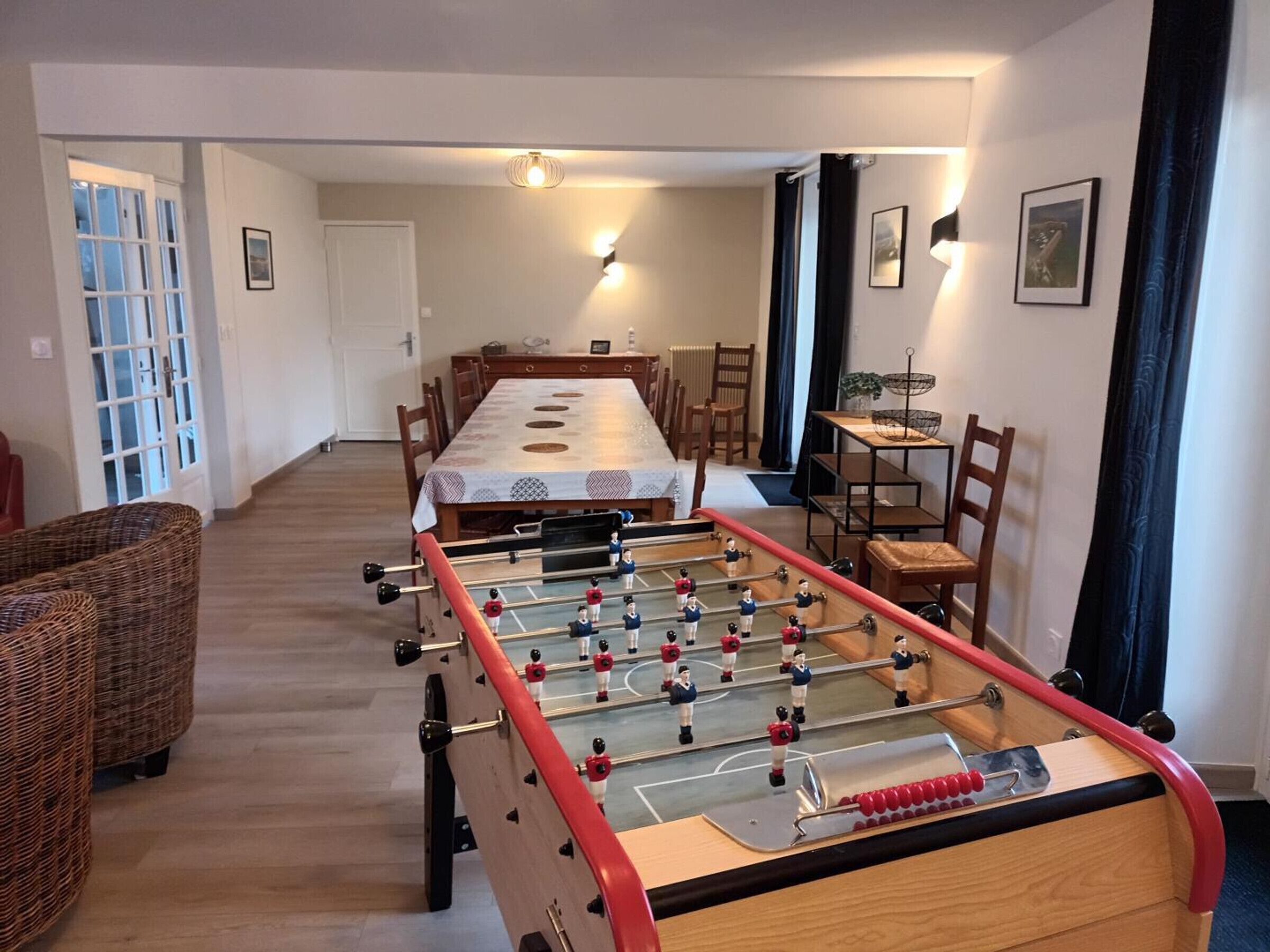 A room with a foosball table, a dining table, and chairs.