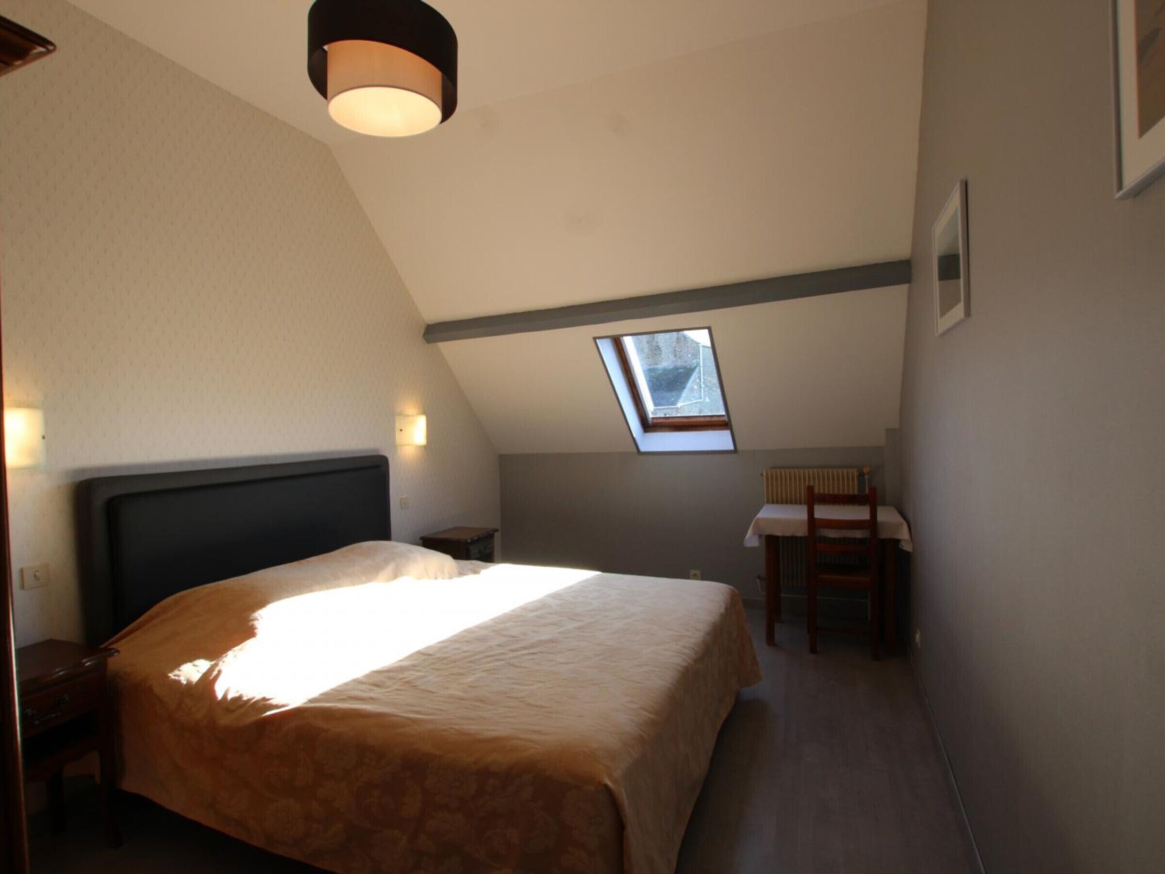 A bedroom with a large bed, a skylight, a desk, and a chair.