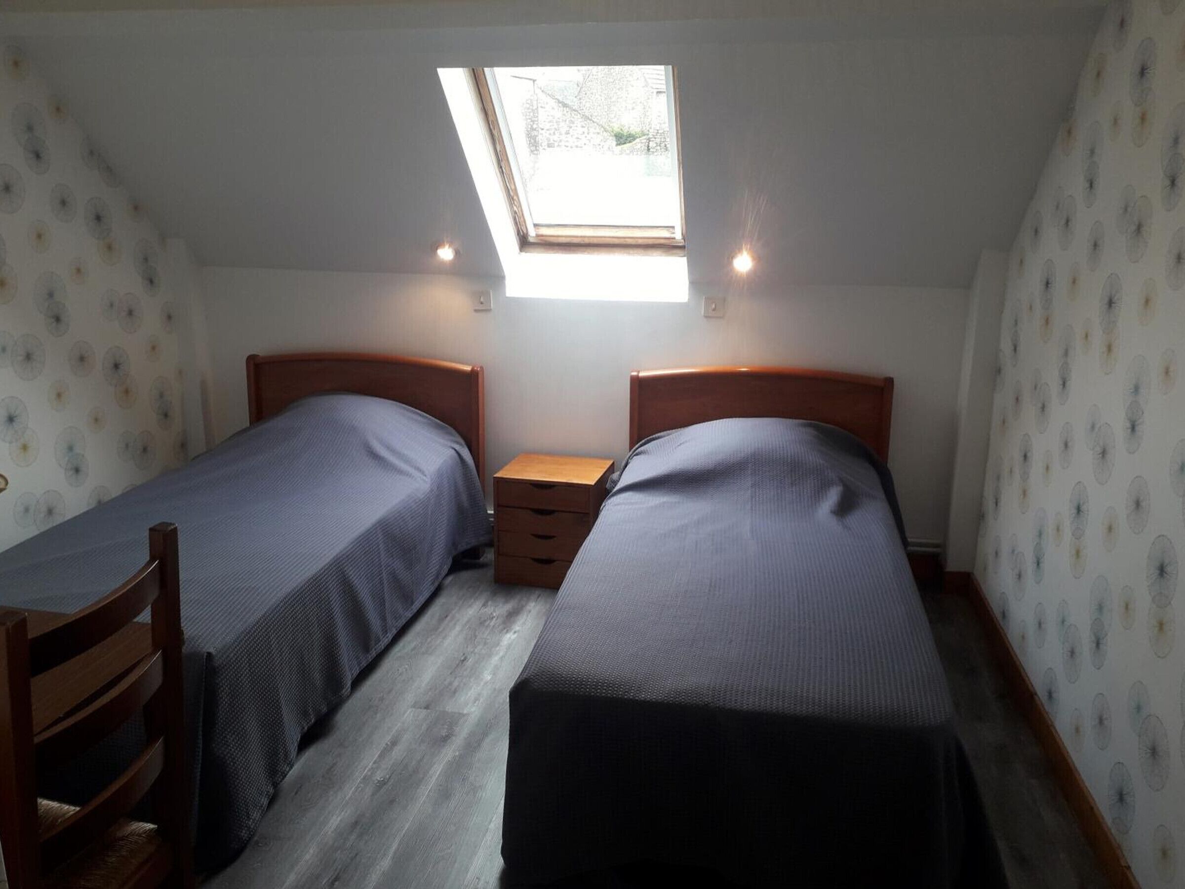 Een kleine, compacte kamer met twee eenpersoonsbedden, een houten nachtkastje en een dakraam.
