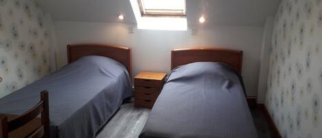 Een kleine, compacte kamer met twee eenpersoonsbedden, een houten nachtkastje en een dakraam.