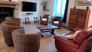 Un salon avec des meubles en osier, un canapé en cuir, un téléviseur à écran plat, une cheminée et une fenêtre avec des rideaux.