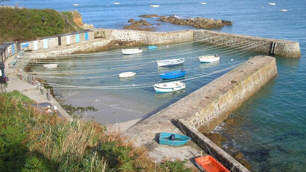 Un port côtier avec des bateaux amarrés et un mur de pierre.