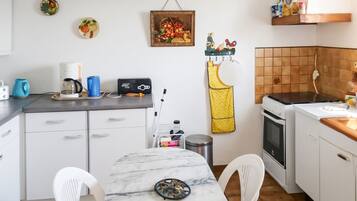 Ett kompakt kök med vita skåp, en bänkskiva i marmor, en spis och ett handfat.
