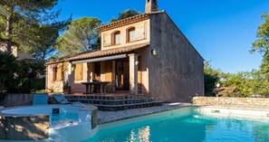 Een villa in mediterrane stijl met een zwembad, terrasmeubilair buiten en een stenen muur.