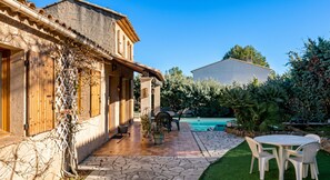 Un patio con piscina, mobiliario exterior y un edificio con techo de tejas.