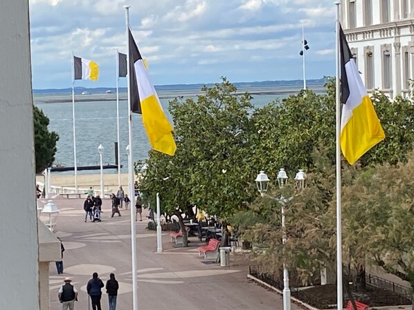 A public square with flags, trees, and a distant view of the sea.