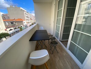 A balcony with a table and chairs, a view of the cityscape, and a large sliding glass door.