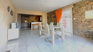 Un'ampia zona giorno con tavolo e sedie, una cucina sullo sfondo e un muro in pietra con una finestra.
