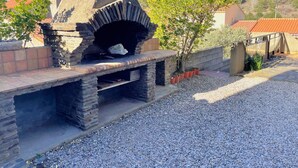 Un forno esterno in pietra con canna fumaria, circondato da ghiaia e piante in vaso.
