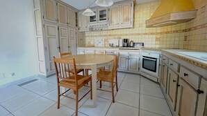 Una cucina con mobili bianchi, un tavolo rotondo in legno e sedie. Sul piano di lavoro si trovano un forno a microonde, una macchina da caffè e un forno.