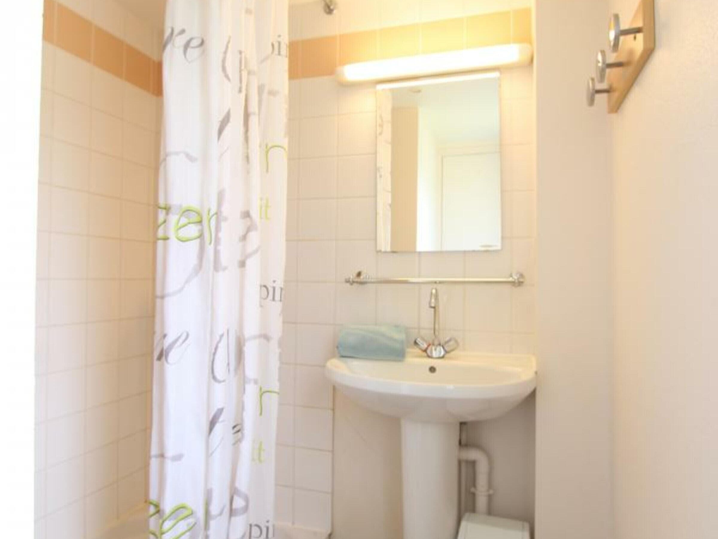 A bathroom with a shower curtain, a sink, a mirror, and a towel rack.