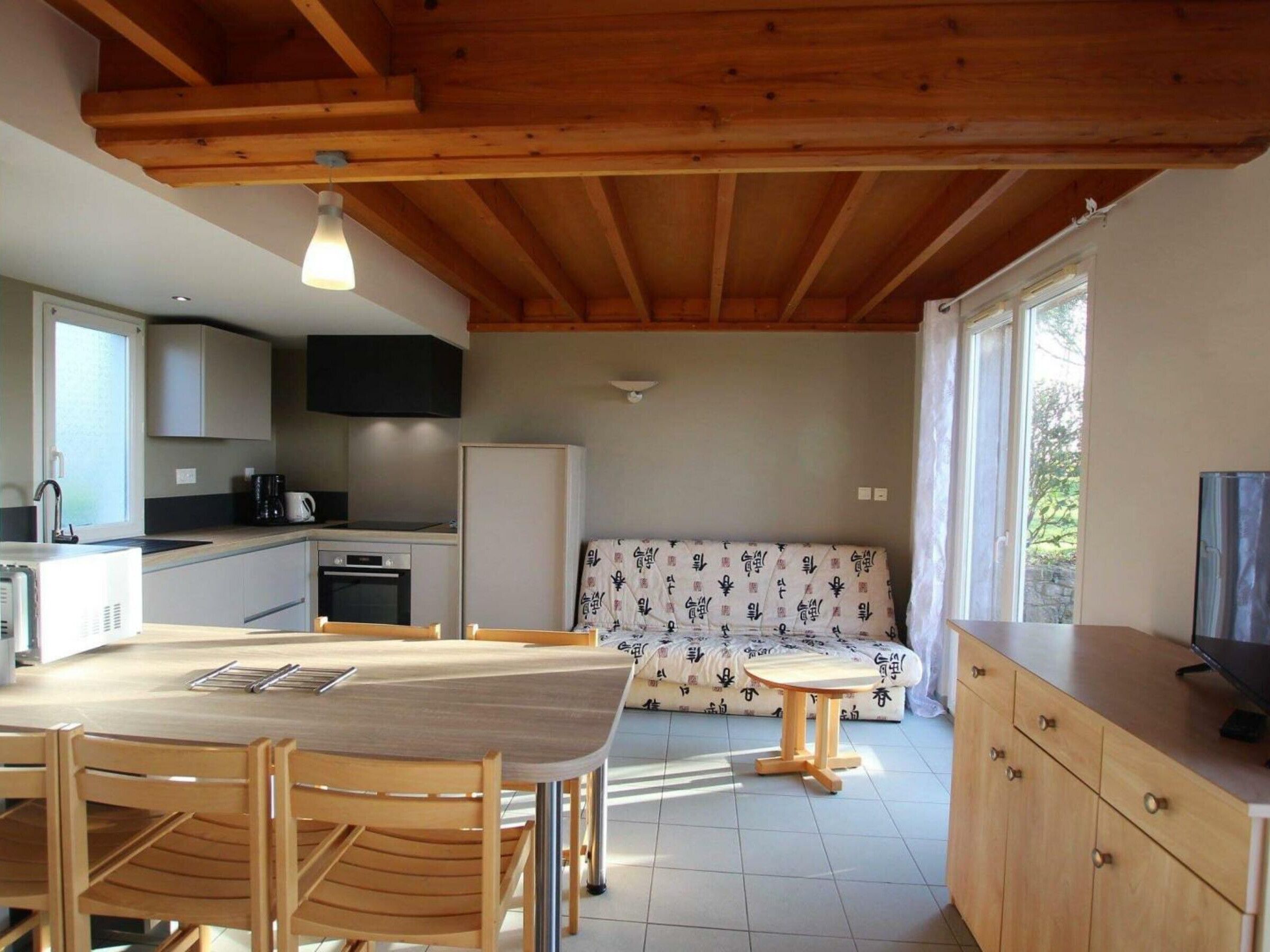 Eine moderne Küche mit Holzbalken, einem Esstisch mit Stühlen, einer Couch und einem Fernseher auf einem Schrank.