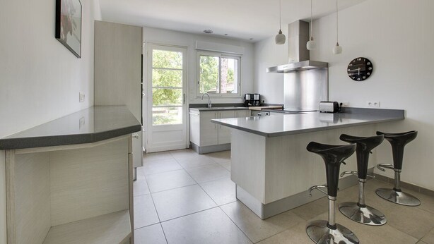 A modern kitchen with a large island, bar stools, and pendant lights.