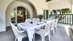 A covered outdoor dining area with a white table set for six, surrounded by white chairs.