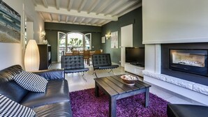 A modern living room with a fireplace, leather sofa, and a dining area in the background.