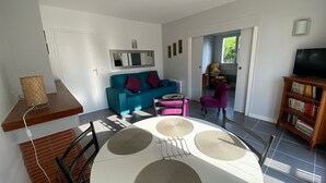 A modern living room with a teal sofa, a coffee table with circular mats, a TV stand with books, and a door leading to another room.